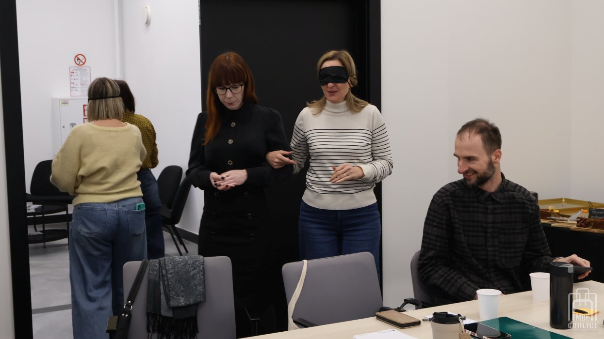 Biblioteka Gorlice, Szkolenie o odstępności ćwiczenie - uczestniczka warsztatów prowadzi koleżankę z zasłoniętymi oczami